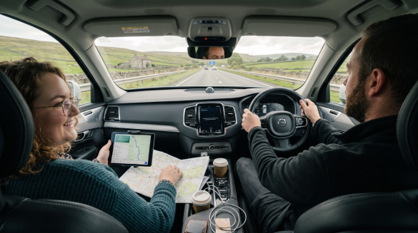 Couple driving scenic road, using map and tablet for navigation, enjoying coffee in modern car interior UK road trip